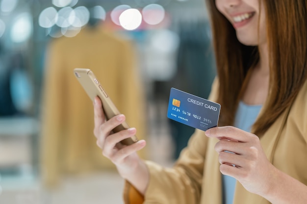 Closeup Asian woman using credit card with mobile for online shopping in department store