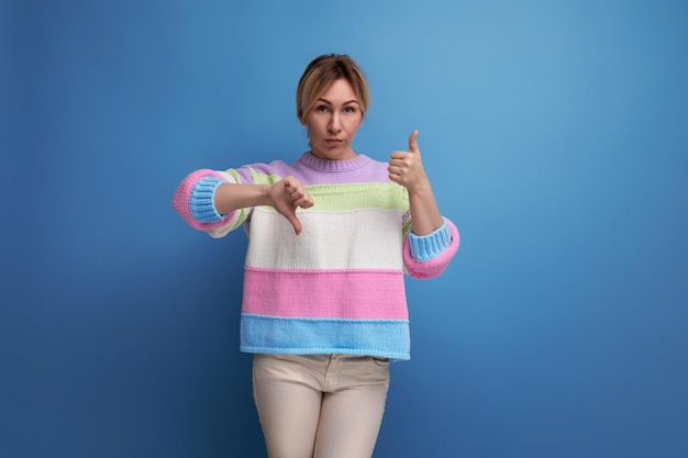 Closeup of an attentive blond young woman in a striped sweater showing like and dislike on a blue