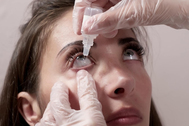 Closeup attentive optometrist dripping eye drops into the patient39s eyes Optometrist during an examination in a modern clinic