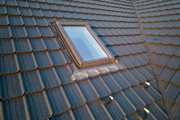 Closeup of attic window on house roof top covered with ceramic shingles Tiled covering of building