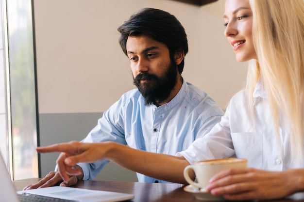 Closeup of attractive business woman looking at laptop screen and explaining points to bearded