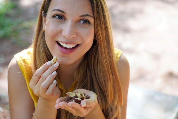 Closeup of attractive healthy woman eating Brazil nuts outoor Looks to the side