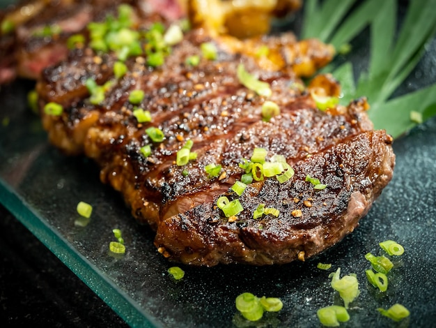 Closeup Australian sliced medium rare wagyu grilled beef steak top with sliced spring onion on glass plate on dark background japanese style Australian grilled meat texture