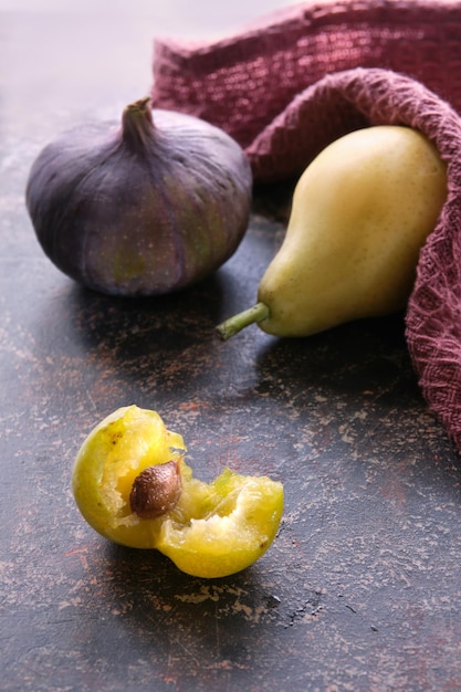 Closeup on Autumn fruits purple fig yellow pear and yellow plums Dark textured brown background and magenta burgundy kitchen towel