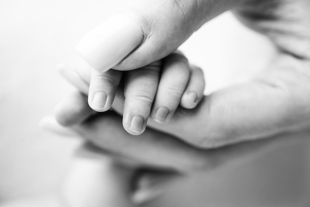 Closeup of a baby39s small hand with tiny fingers and arm of mother Newborn baby holding the finger of parents after birth The bond between mother and child Happy family concept Black and white