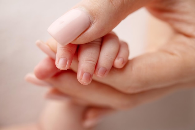 Closeup of a baby39s small hand with tiny fingers and arm of mother on a white background Newborn baby holding the finger of parents after birth The bond between mother and child Happy family concept