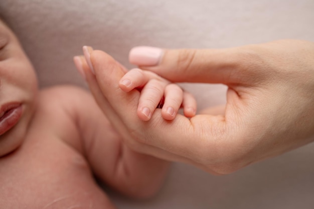 Closeup of a baby39s small hand with tiny fingers and arm of mother on a white background Newborn baby holding the finger of parents after birth The bond between mother and child Happy family concept