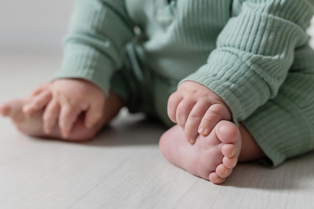 closeup of the bare feet of a baby in a green jumpsuit sitting on the floor