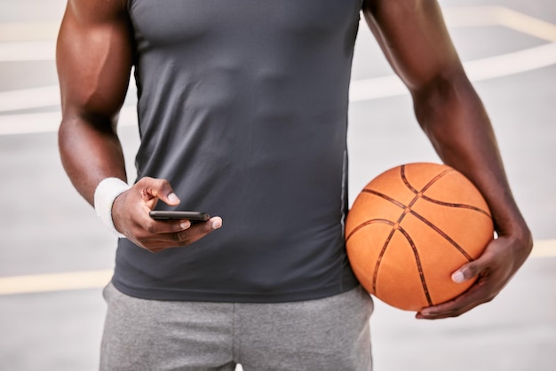 Closeup of a basketball player texting on a phone while taking a break from playing a match on a sports court outside Hands of one male athlete browsing social media online during a game interval