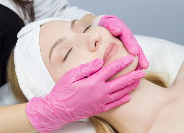 A closeup beautician does rejuvenating facial treatments for female clients at a spa or salon A cosmetologist gives a patient a facelift massage in the clinic of aesthetic medicine Beauty cosmetology