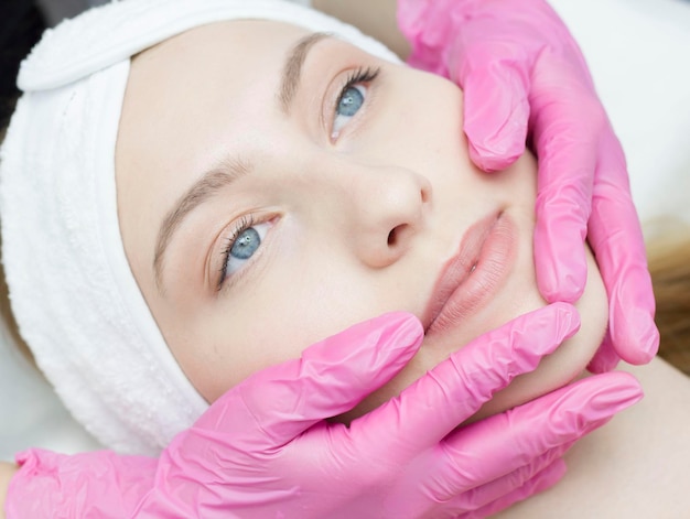 A closeup beautician does rejuvenating facial treatments for female clients at a spa or salon A cosmetologist gives a patient a facelift massage in the clinic of aesthetic medicine Beauty cosmetology