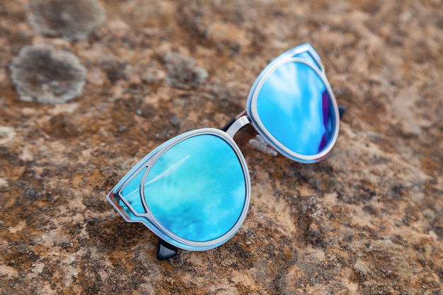 Closeup beautiful blue green mirrored sunglasses ultraviolet on ground in sunshine at sunset, reflection of stones, limestone, vineyard.  fashion shooting accessories for an optics store