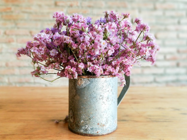 Closeup beautiful violet flowers in zinc vintage vase on wooden table and blurred brick wall 