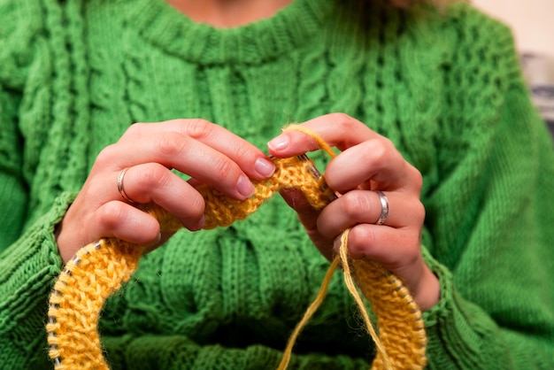 Photo closeup of a beautiful woman in knitting green sweater knitting needles from a natural woolen thread a yellow hat a woman shows how to knit correctly