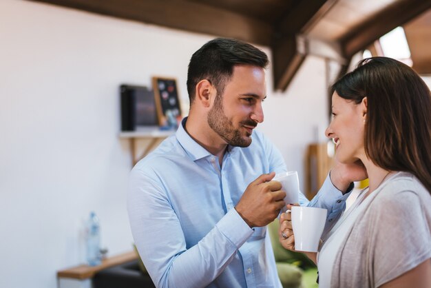 Closeup of beautiful young couple looking at each other and smiling while enjoying coffee in cafe together