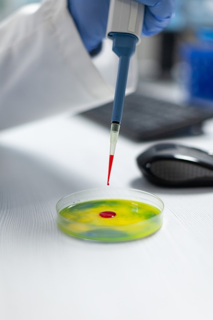 Closeup of biologist researcher man hands dropping red liquid in petri dish