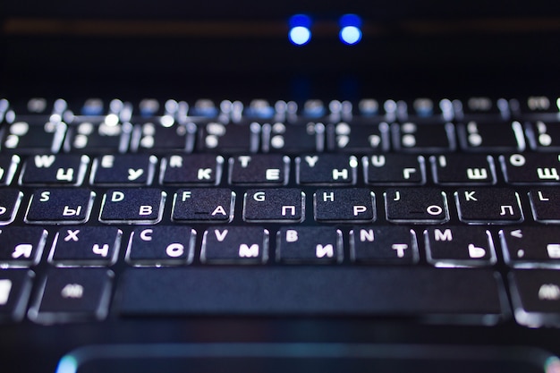 Closeup of black notebook laptop keyboard with english and russian illuminated letters