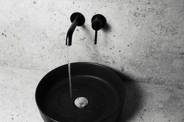 Closeup of black sink and wall mounted faucet with flowing water Top view