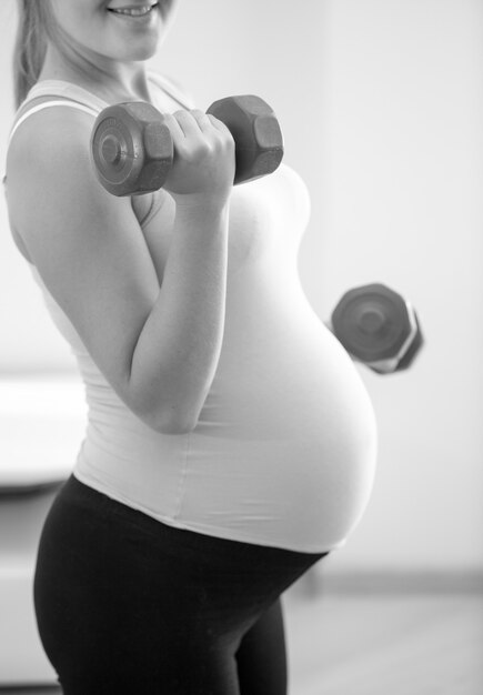 Closeup black and white photo of pregnant woman lifting dumbbells