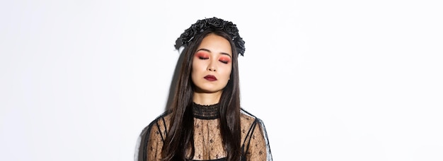 Closeup of bored asian woman sleeping while standing over white background in witch costume