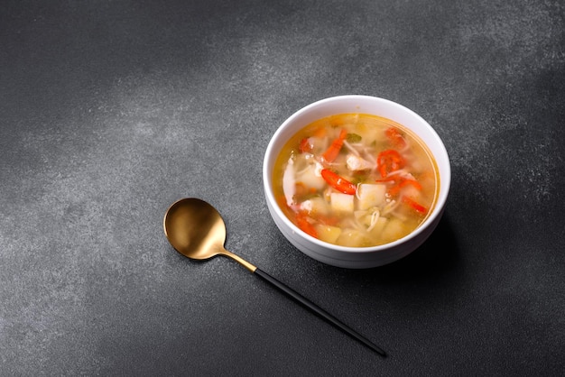 Closeup of a bowl of chicken noodle and vegetable soup on a concrete table