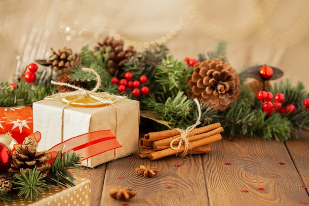 Closeup of a box with a gift wrapped in kraft paper and a Christmas background with a Christmas tree decorated with decorative balls with golden lights on a wooden table cinnamon sticks copy space