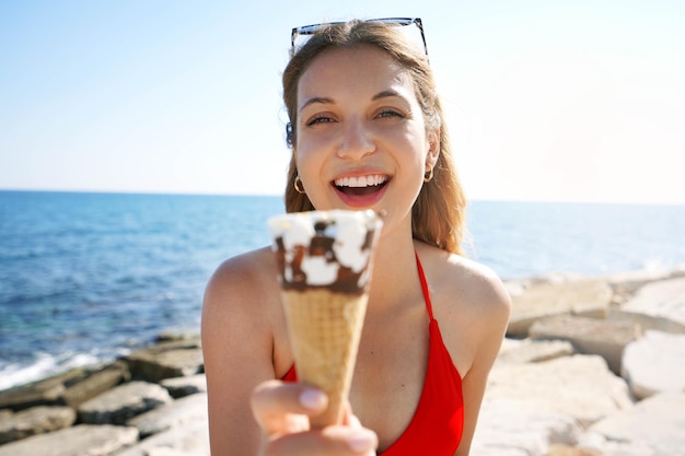 Closeup of Brazilian woman smiling at camera showing ice cream cone on the beach on summertime