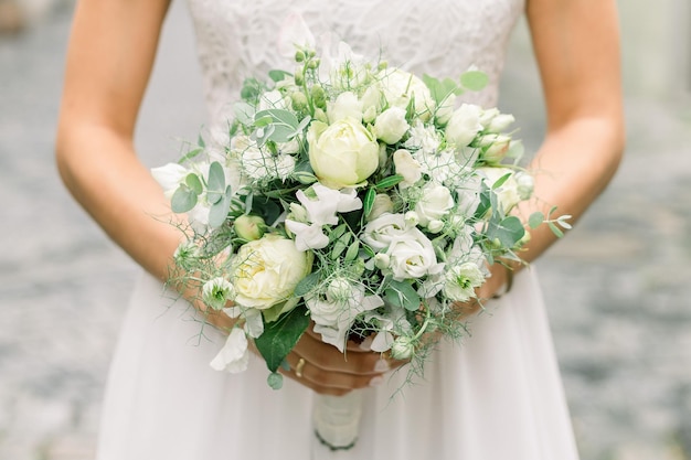 Closeup of bride with white dress holding wedding bouquet with roses