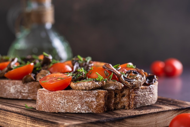 Closeup of bruschetta on rye bread with cherry tomatoes and fried mushrooms on a wooden board