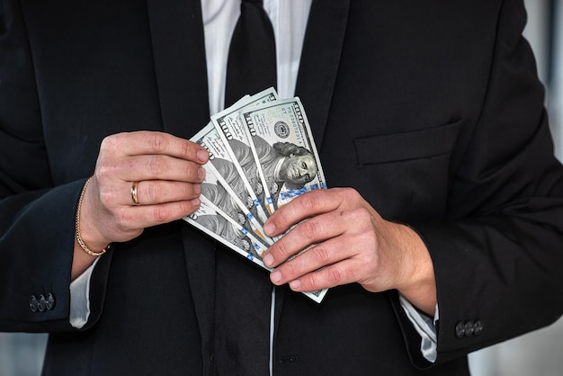 Closeup of businessman's hand in branded suit holding dollar banknotes The concept of very profitable investment