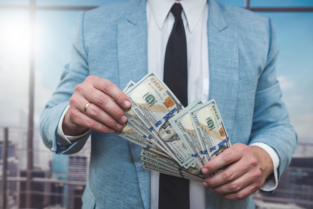 Closeup businessman in suit holding one hundred 100 dollar bill