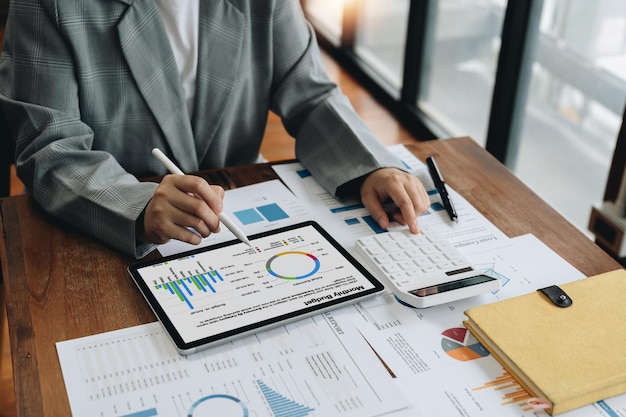 Closeup of businesswoman analyzing financial report with calculator and digital tablet at wooden desk