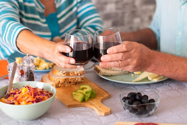 Closeup on caucasian senior couple sitting at the table having brunch at home toasting with glasses of wine