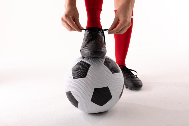 Photo closeup of caucasian young female player tying soccer shoe lace while standing with foot on ball