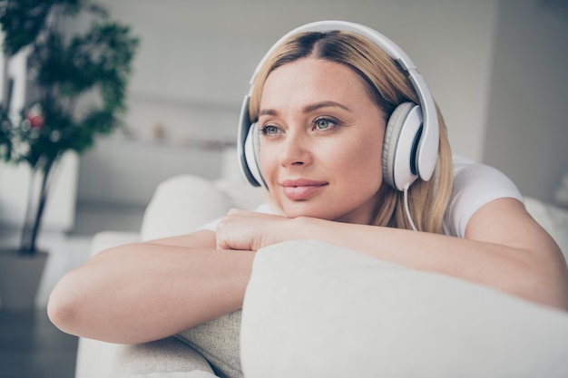 closeup charming lady sit comfy couch chin on hands listen earphones dream