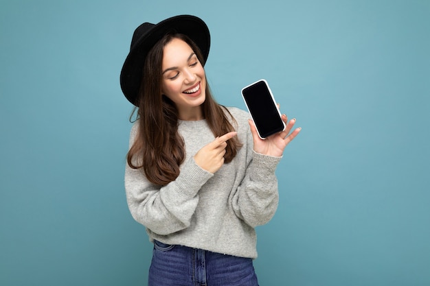 Closeup of charming young happy woman wearing black hat and grey sweater