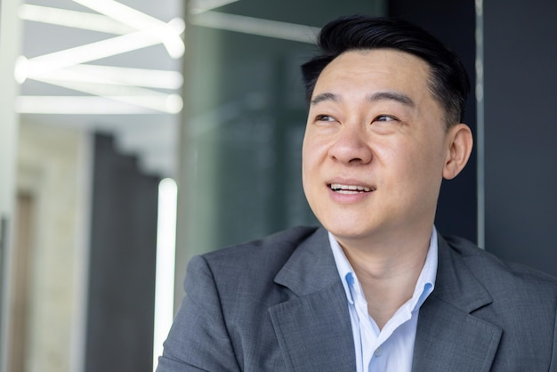 Closeup of a cheerful asian businessman in formal wear looking away thoughtfully in a bright office