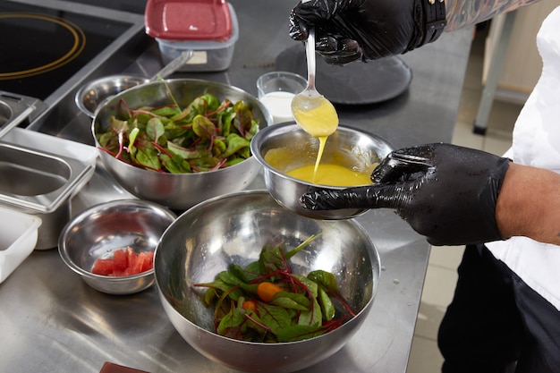 Closeup of chef hands preparing salad pouring sauce in a restaurant kitchen