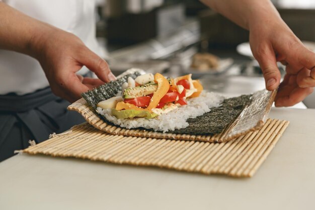 Closeup of Chef hands rolling up sushi on bamboo mat in kitchen of restaurant