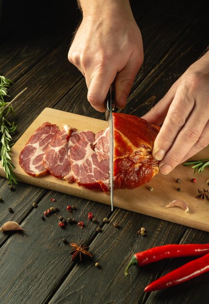 Photo closeup of a chef hands with a knife cuts smoked veal meat into thin slices for a sandwich fast food concept on dark background