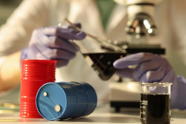 Closeup of chemist holding flask with oil at research laboratory oil barrels scientific