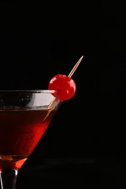 Closeup on cherry with red drink in martini glass and dark background