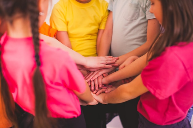 Closeup children's hands closely one over another Kids standing close holding hands in large tight knot Teamwork and connection concept