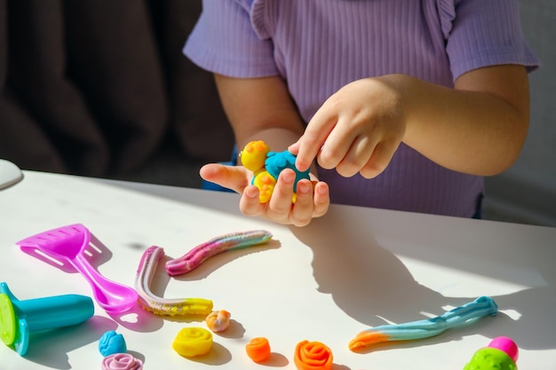 Closeup children's hands with plasticine turtle on white table at home children's motor skills development games children with plasticine