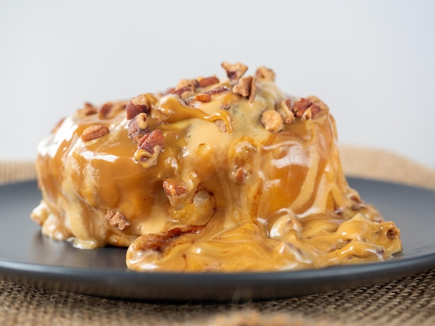 Closeup of a cinnamon bun topped with caramel topping and pecans Black plate side view Delicious sweet dessert blurred background Selective focus