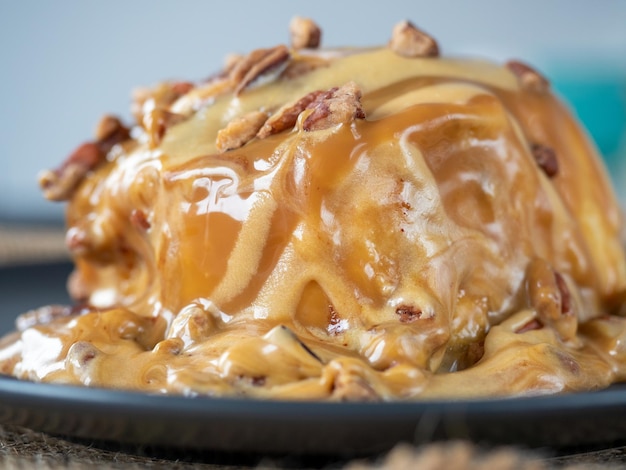 Closeup of a cinnamon bun topped with caramel topping and pecans Black plate side view Delicious sweet dessert