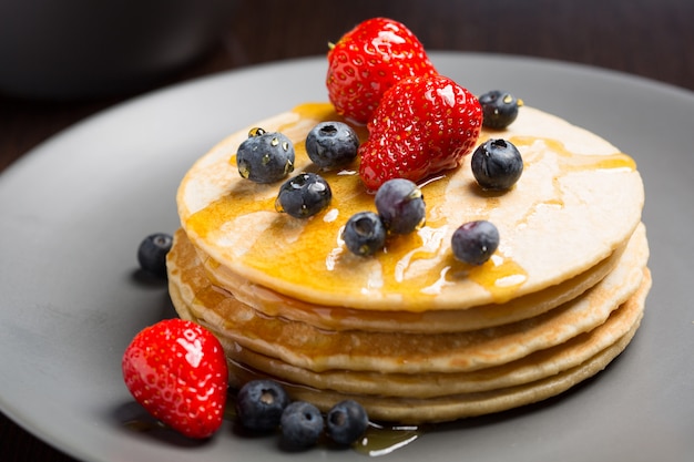 Closeup of classic american pancakes, with strawberries and fresh blueberries and syrup.