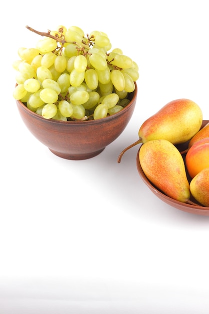 Closeup of colorful grapes and pears on a clay plate Bunches of grapes and pears isolated on white background