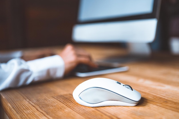 Closeup of a computer mouse on a table against the background of a working girl at a computer dresse...