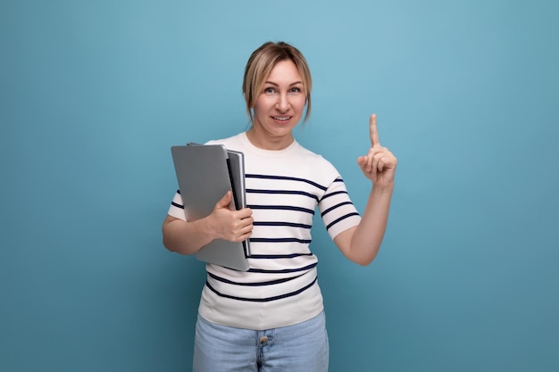 Closeup of a confident blonde woman in a striped sweater holding a laptop in her hands on a blue